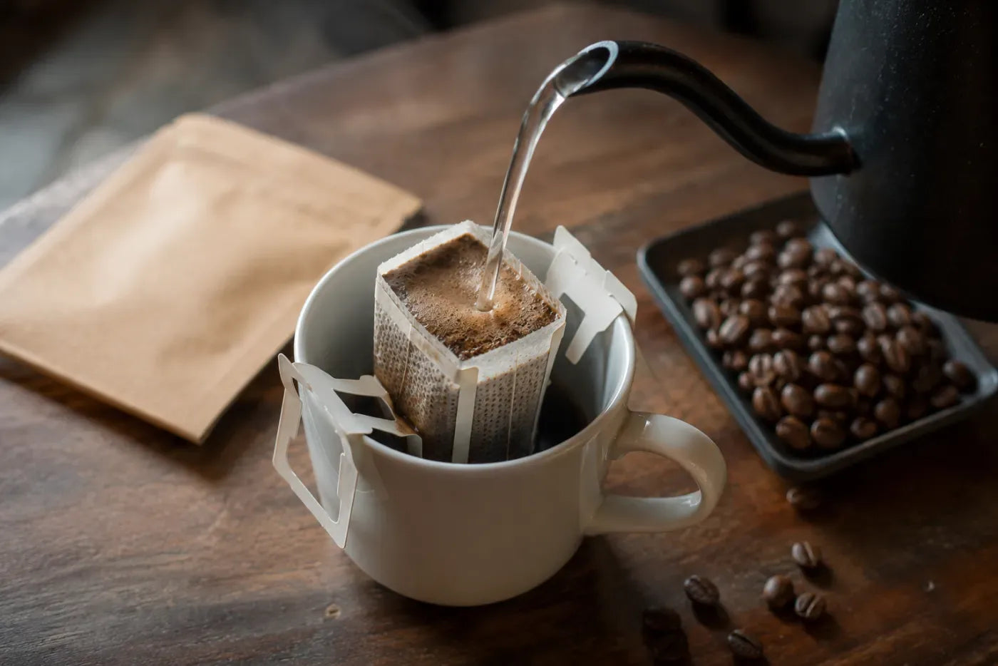 Drip Bag über eine weiße Tasse gehängt und mit heißem Wasser aus einem Wasserkessel aufgebrüht